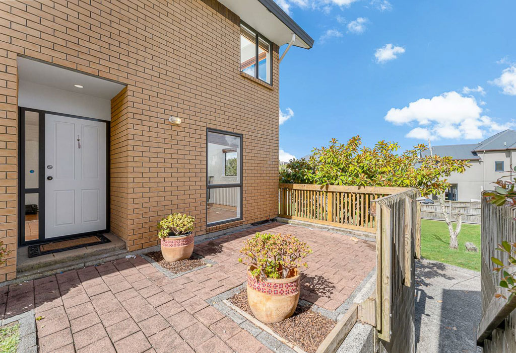 Welcoming front courtyard of brick Albany townhouse with paved entry, landscaped garden, and secure fencing – perfect low-maintenance North Shore home.