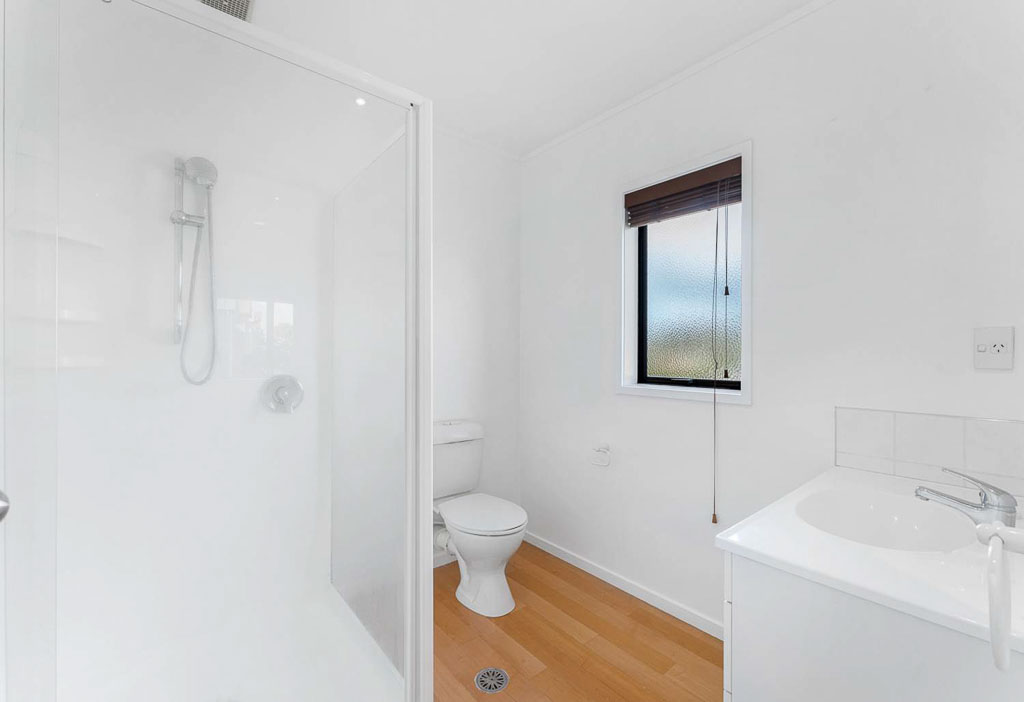 Contemporary bathroom in Rangitoto College Zone property with glass shower, toilet, and fresh white interior – ideal for first home buyers.