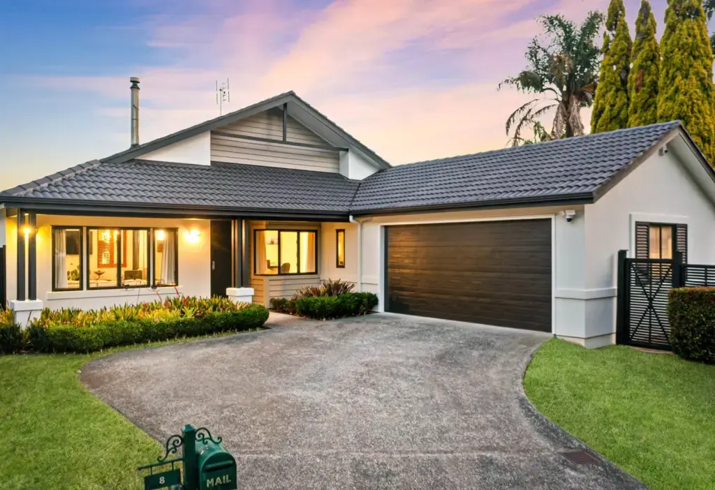 Single-level family home with double garage and landscaped garden at sunset, marketed by Real Estate Agent in Albany Michael Hossaini, Barfoot & Thompson.
