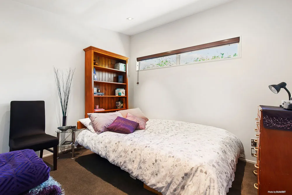 Cosy bedroom featuring a wide horizontal window, neutral walls, a wooden bookcase, and soft natural light.