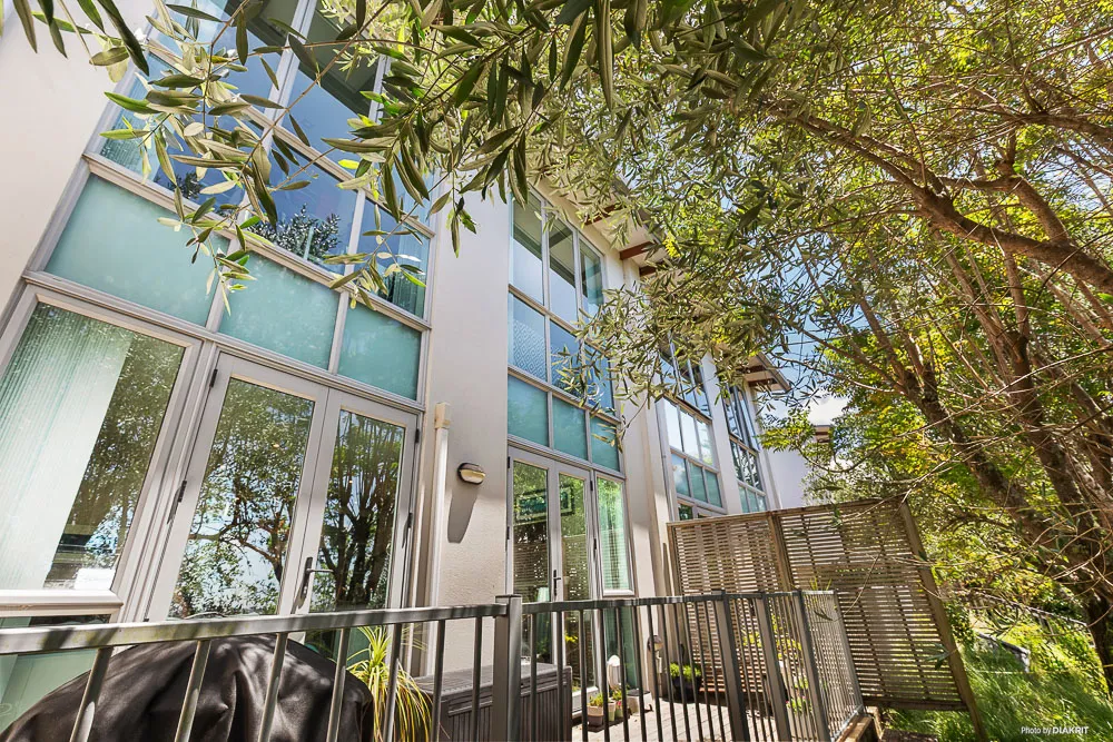 Exterior view of 5-20 Schnapper Rock Road showcasing full-height windows, modern architectural lines, and a private deck surrounded by mature trees and lush greenery.