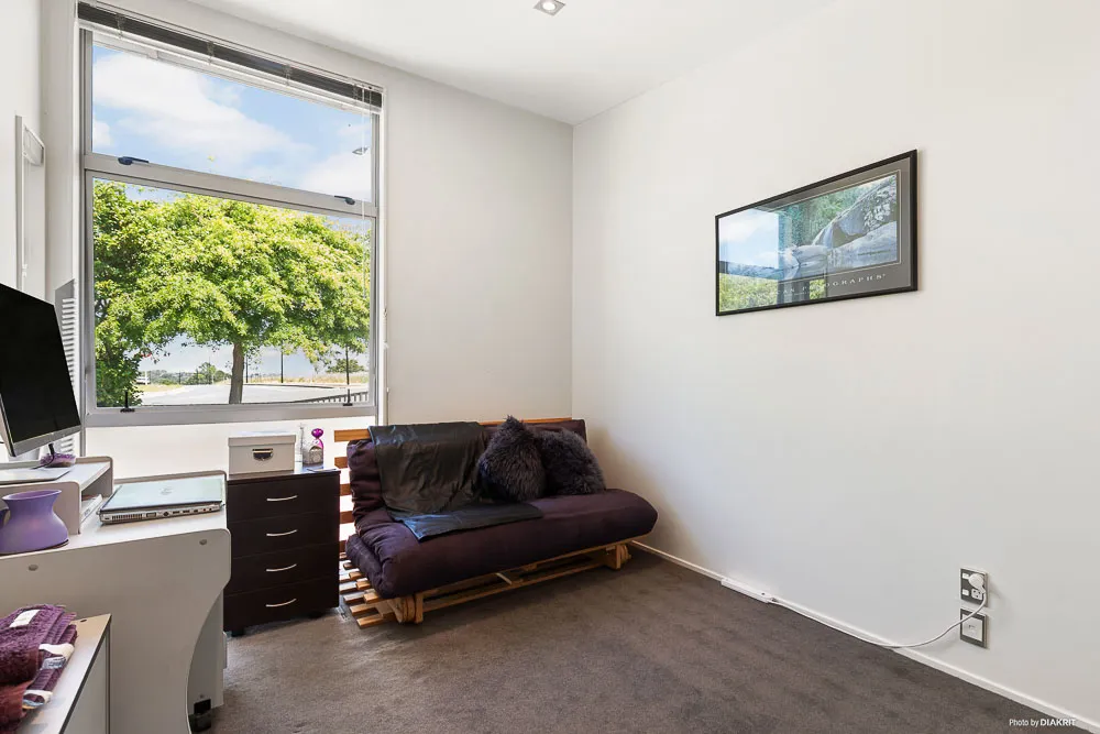Bright second bedroom at 5-20 Schnapper Rock Road featuring a large picture window with leafy street views, neutral walls, and space for a desk or sofa bed.